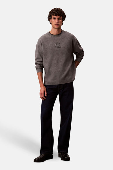 Sweat-shirt gris avec col rond de Calvin Klein, avec des manches longues et un jeans foncé.