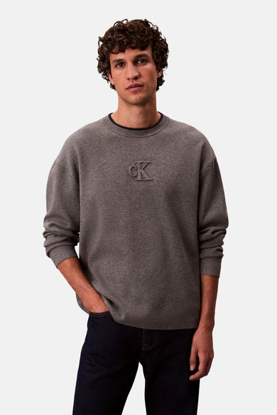 Sweat-shirt gris avec col rond de Calvin Klein, avec logo CK en relief, porté avec des jeans foncés.