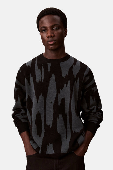 Sweat-shirt multicolore à col rond de Calvin Klein, avec un motif abstrait, associé à un pantalon noir et des chaussures noires.