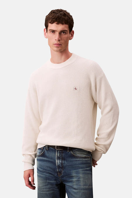 Beige trui met ronde hals van Calvin Klein, met een fijn gebreide textuur en lange mouwen, gedragen met jeans.

