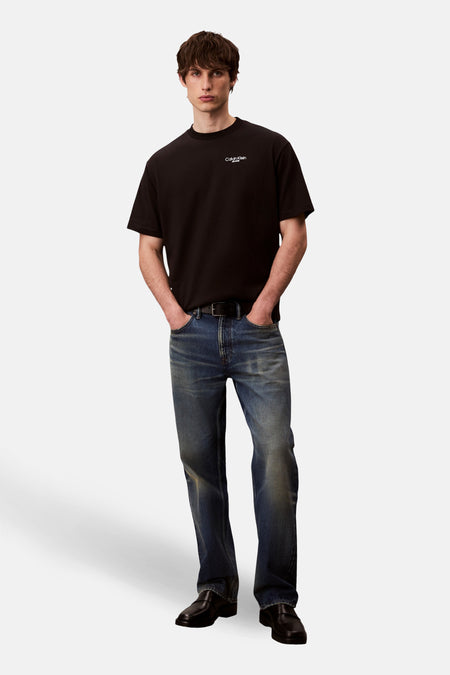 Zwart T-shirt met korte mouwen van Calvin Klein Jeans, gedragen met een donkerblauwe jeans en zwarte schoenen.
