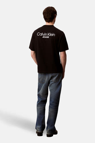 T-shirt noir à manches courtes de Calvin Klein Jeans, avec logo blanc sur le dos et jeans bleus.