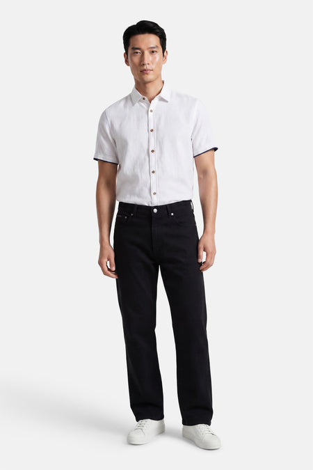 Jean droit noir de Calvin Klein, porté par un homme avec une chemise blanche et des baskets blanches.