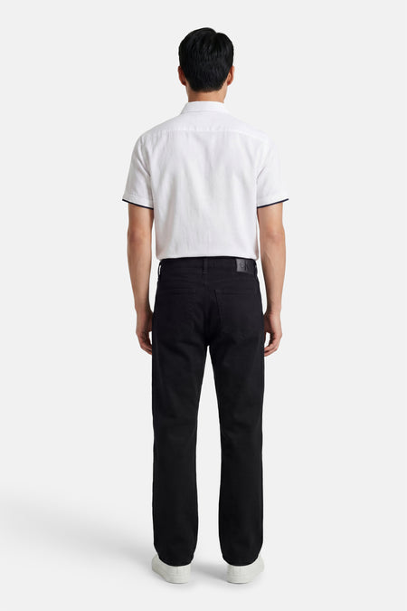 Zwarte straight fit spijkerbroek van Calvin Klein, met zichtbare CK-patch, gedragen door een man met een wit shirt en sneakers, achterkant.