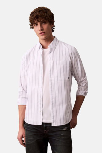 Wit gestreept overhemd met lange mouwen van Calvin Klein, gedragen over een wit T-shirt en donkere jeans.
