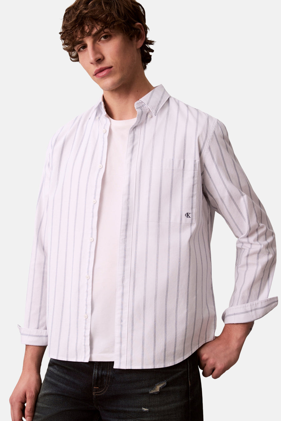 Wit, gestreept overhemd met lange mouwen van Calvin Klein, met een borstzak en gedragen over een wit T-shirt, gecombineerd met jeans.