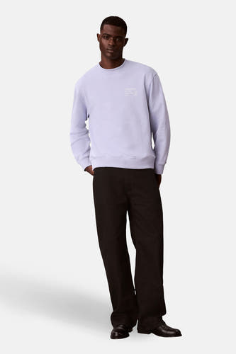 Pull-over marron avec col rond de Calvin Klein, imprimé texte, associé à un pantalon noir et des chaussures.