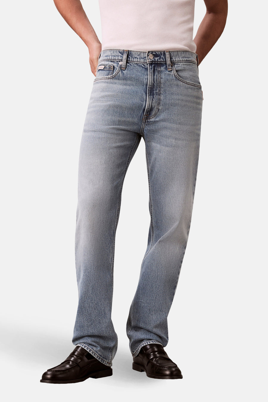 Jeans coupe droite bleu clair en denim de Calvin Klein, combinés avec des mocassins noirs en cuir et une chemise blanche.