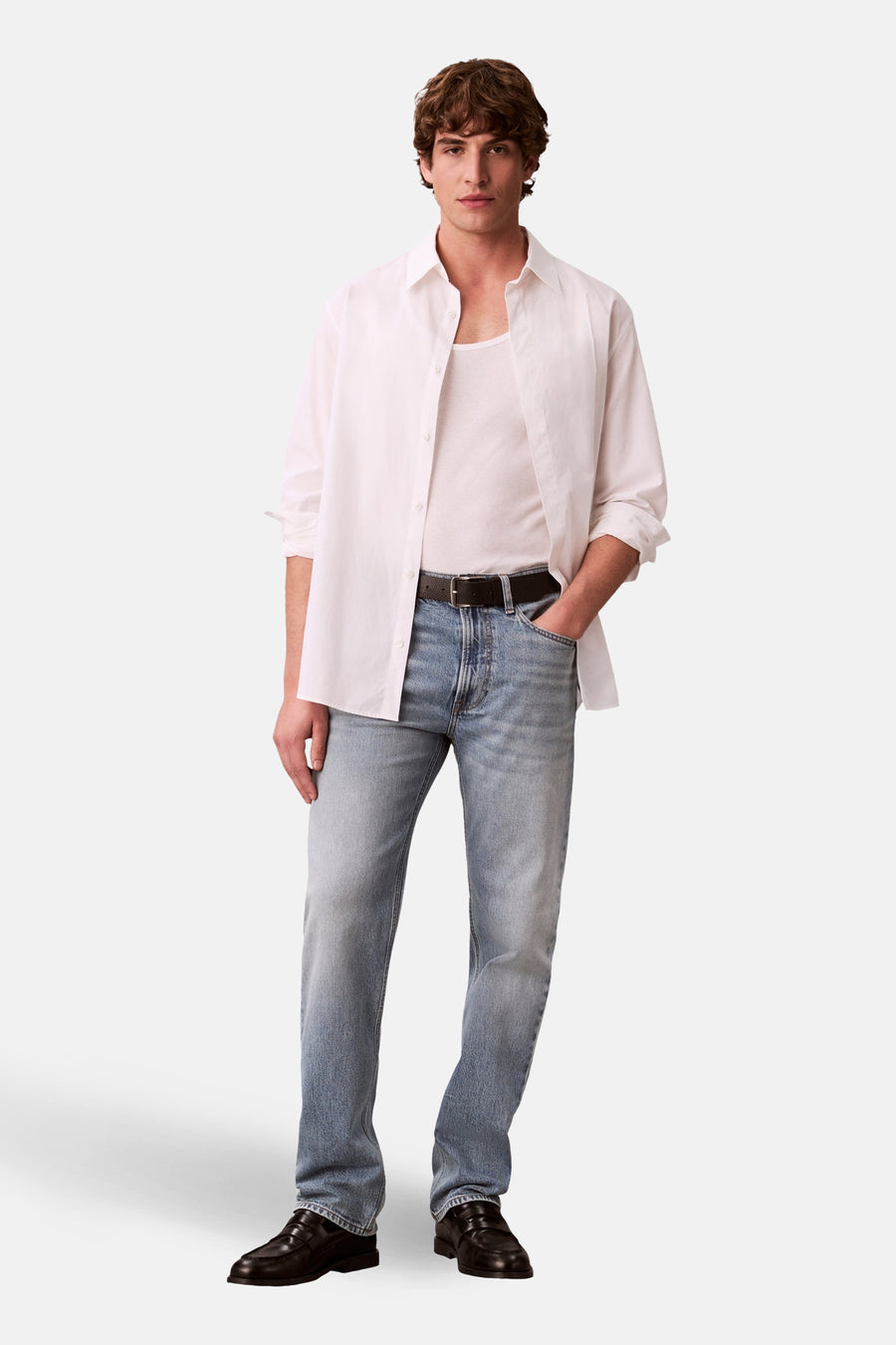 Jean droit en denim bleu clair de Calvin Klein, avec une ceinture noire, combiné avec une chemise blanche.