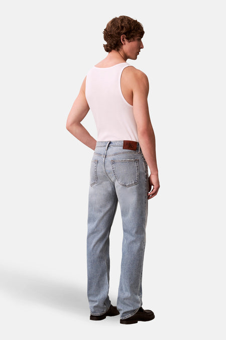 Jeans straight light blue denim van Calvin Klein, achterkant gezien, gecombineerd met een wit hemd en zwarte schoenen.

