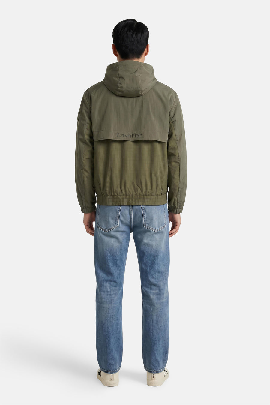 Kaki korte jas van Calvin Klein, achterkant met capuchon en logo, gestreept patroon, model draagt blauwe jeans