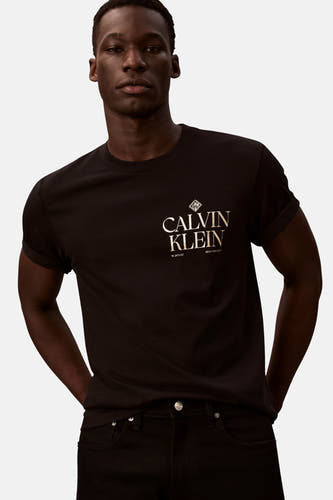 T-shirt noir à manches courtes de Calvin Klein, avec logo or sur la poitrine, porté avec un jean noir.
