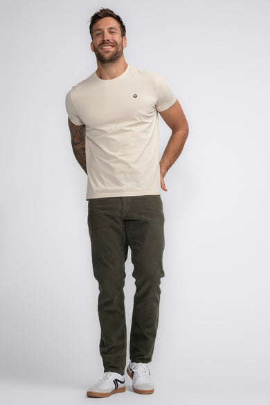 T-shirt écru à manches courtes de Petrol Industries, avec un petit logo sur la poitrine, associé à un pantalon kaki et des baskets blanches.