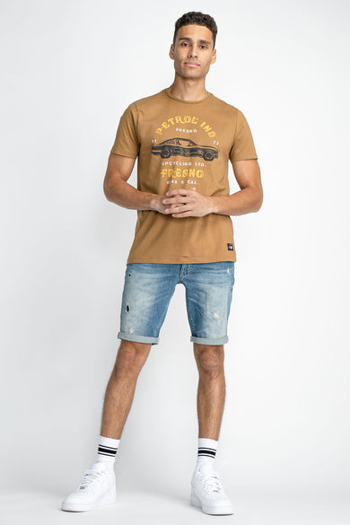 Blauwe jeansshort van Petrol Industries, met gerafelde details en opgerolde pijpen, gedragen met witte sneakers en sokken.
