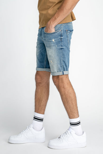 Blauwe jeansshort van Petrol Industries, met rolled-up zoom en gedragen met witte sokken en sneakers.
