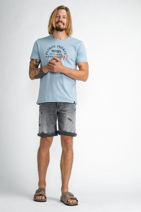 Donkerblauwe jeansshort van Petrol Industries, met een vervaagde wassing en opgerolde pijpen, gecombineerd met een lichtblauw T-shirt en suède sandalen.