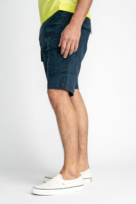 Blauwe cargo shorts van Petrol Industries®, zijprofiel, met grote zakken en opgerolde zoom, gedragen met gele top en witte sneakers