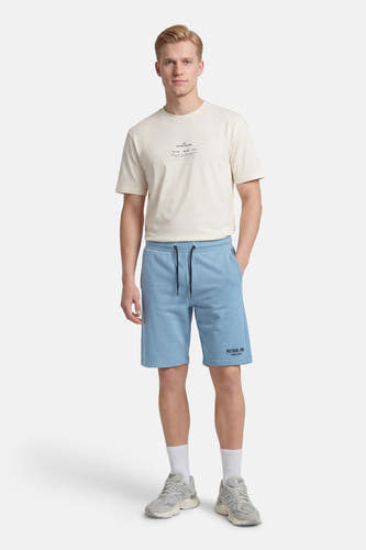 Blauw short van Petrol Industries, met trekkoord en logo, gecombineerd met een crèmekleurig T-shirt en grijze sneakers met witte sokken.
