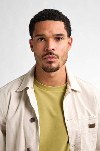 Portret van man in beige jas en groene trui tegen witte achtergrond.