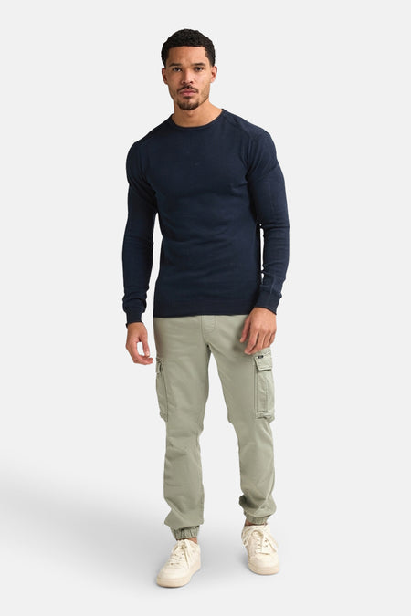 Blauwe trui met ronde hals van Petrol Industries, gedragen met kaki cargobroek en crèmekleurige sneakers.
