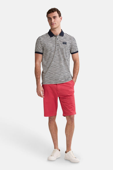 Polo rayé bleu avec manches courtes de Petrol Industries, associé à un short rouge et des baskets blanches.