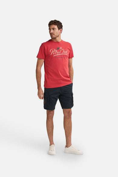 Zwarte bermuda van Petrol Industries met zakken op de zijkant, gecombineerd met een rood T-shirt en witte sneakers.
