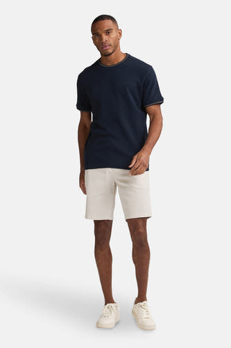 Beige short van Petrol Industries®, gecombineerd met een donkerblauw T-shirt en witte sneakers.