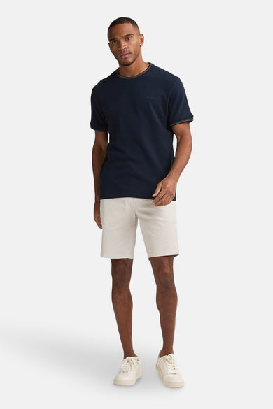 Beige short van Petrol Industries®, gecombineerd met een donkerblauw T-shirt en witte sneakers.