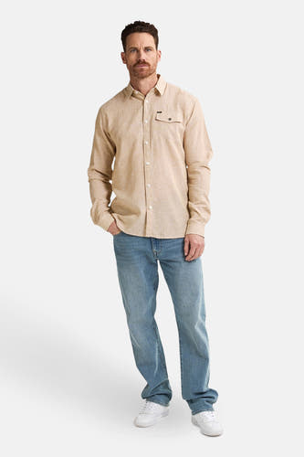 Beige hemd met lange mouwen van Petrol Industries, met borstzak en gedragen met blauwe jeans en witte sneakers.
