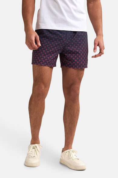 Blauwe zwemshort van Petrol Industries® met rood waaierpatroon, gedragen met een wit T-shirt en crèmekleurige sneakers.