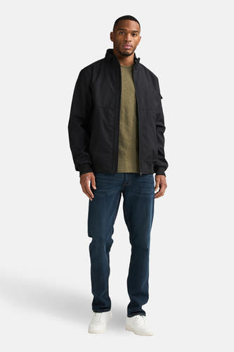 Zwarte korte jas van Petrol Industries®, gecombineerd met een olijfgroen T-shirt, donkerblauwe jeans en witte sneakers.
