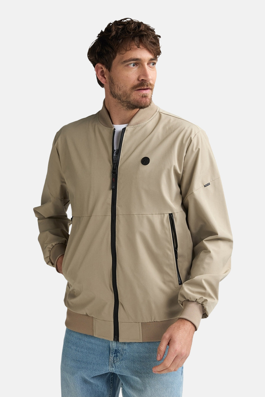 Beige korte jas van Petrol Industries®, met zwarte rits en zakken, gedragen met blauwe jeans.
