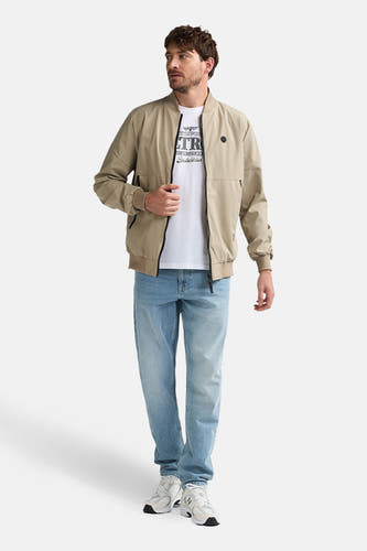 Beige korte jas van Petrol Industries®, met rits en gedragen met een wit T-shirt en blauwe jeans.