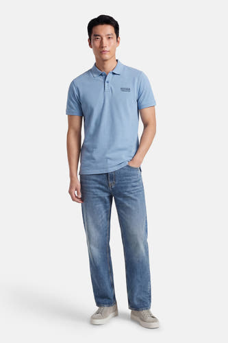 Blauwe polo van Petrol Industries, met korte mouwen, gedragen met jeans en grijze sneakers.
