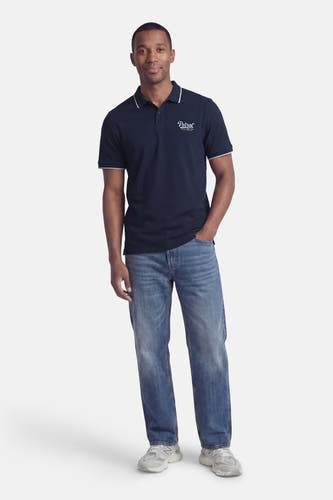 Blauwe polo van Petrol Industries met witte accenten op de kraag en mouwen, gecombineerd met jeans en sneakers.
