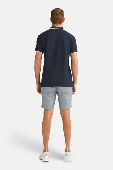 Blauwe short van Petrol Industries®, gecombineerd met een donkerblauw poloshirt en witte sneakers, gezien van achteren.