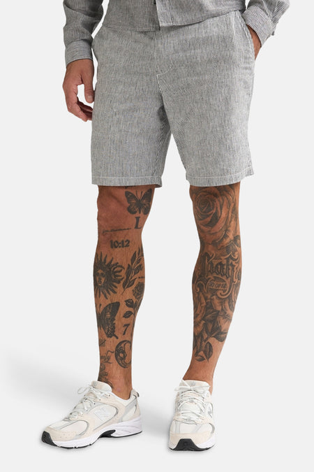 Lichtgrijze short met pinstripes van Petrol Industries, gedragen door een man met tattoos en witte sneakers.