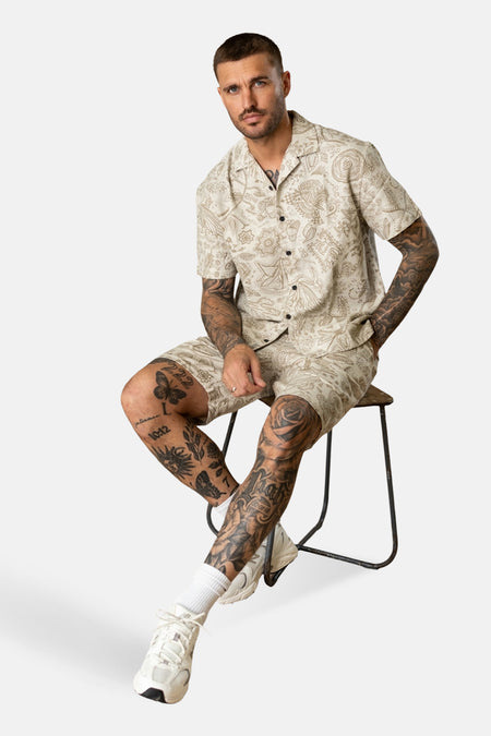 Ecru hemd met korte mouwen van Petrol Industries, met paisley-motief, gedragen met bijpassende shorts en witte sneakers.