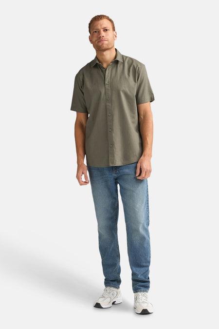 Groen overhemd met korte mouwen van Petrol Industries, gecombineerd met blauwe jeans en witte sneakers.