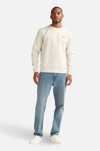 Ecru sweater met ronde hals van Petrol Industries, met lange mouwen en lichtblauwe jeans en witte sneakers.