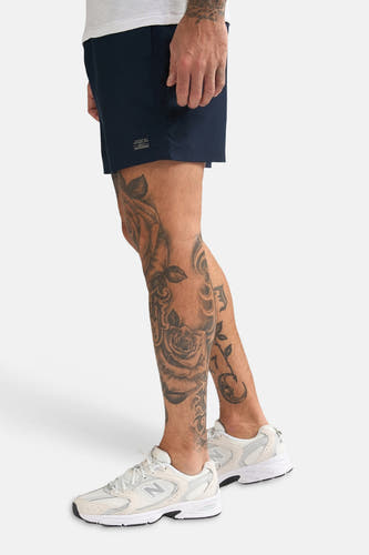Blauwe zwemshort van Petrol Industries, met korte pijpen en verder een getatoeëerde man met witte schoenen.
