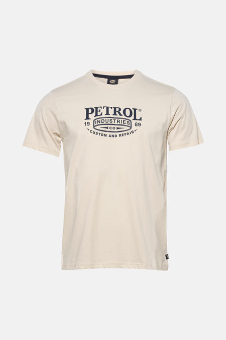 T-shirt écru à manches courtes de Petrol Industries, avec un imprimé logo et porté avec un jean gris et des baskets de couleur crème.