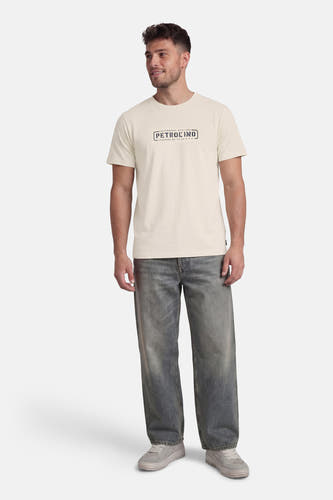 Ecru T-shirt met korte mouwen van Petrol Industries, met een logo op de borst, gecombineerd met grijze jeans en grijze sneakers.