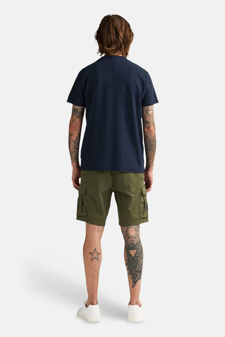 Blauw T-shirt met korte mouwen van Petrol Industries, met een textuur en gedragen met groene shorts en witte sneakers, gezien van achteren.

