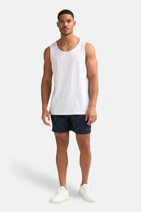 Débardeur blanc de Petrol Industries, porté par un homme avec un short bleu foncé à imprimé oiseau et des baskets blanches.