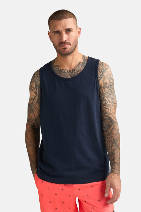 Débardeur bleu de Petrol Industries, montré de dos sur un homme tatoué portant un short couleur corail et des baskets blanches.