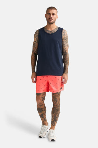 Blauwe singlet van Petrol Industries, gedragen door een getatoeëerde man met koraalrode shorts met ankermotief en witte sneakers.