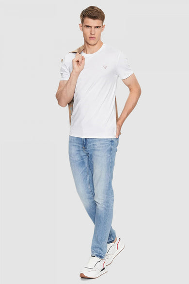 Wit T-shirt met korte mouwen van Guess, met een jas over de schouder en lichte jeans en witte sneakers.
