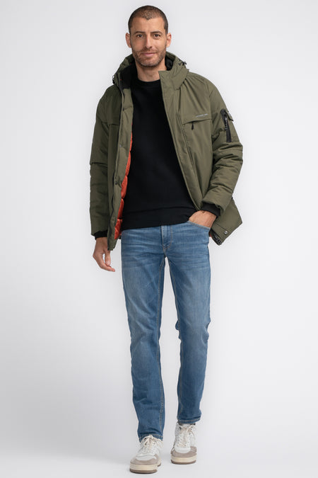 Khaki regenjas van Petrol Industries, gedragen met een zwarte trui en blauwe jeans, in een staande positie.

