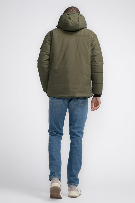 Khaki regenjas van Petrol Industries, rugaanzicht met capuchon, gecombineerd met spijkerbroek en sneakers.
